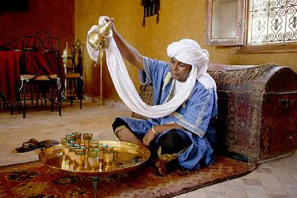 Homme en tenue traditionnelle servant le thé de haut, assis devant un plateau de verres