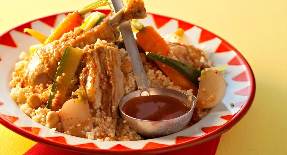 Couscous au poulet et aux légumes servi dans une assiette, avec sa louche de bouillon