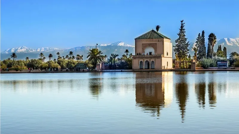 Le bassin de la Ménara et son pavillon au toit de tuiles vertes, reflétés dans l’eau, avec les sommets enneigés du Haut Atlas en arrière-plan